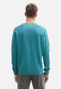 Türkiser Strickpullover mit runder Ausschnitt, gerippten Bündchen und Saum. Weiche Textur, lockere Passform und minimale Details auf der Rückseite.