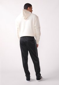 Light cream hoodie with a drawstring hood and contrasting seams, paired with black track pants featuring white side stripes and elastic waistband.
