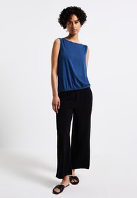 Niebieska bezrękawnikowa bluzka z marszczonym pasem, połączona z czarnymi spodniami o szerokich nogawkach. Gładki materiał o miękkiej teksturze, charakteryzujący się minimalistycznym wzornictwem.