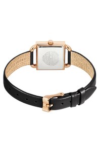 Montre en or rose avec un boîtier métallique rectangulaire et un bracelet en cuir noir. Le bracelet présente une doublure intérieure texturée avec un motif géométrique.