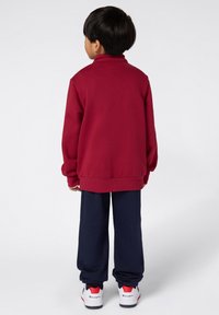 Bordeaux sweatshirt met hoge kraag, gecombineerd met marineblauwe joggers. Kenmerkt zich door een relaxte pasvorm en geribde manchetten, aangevuld met witte en rode sneakers.