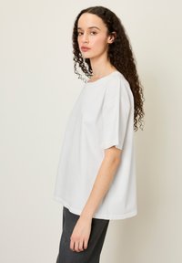 T-shirt en coton blanc avec une coupe décontractée, un col rond et des manches courtes, présentant une texture lisse et un design minimaliste.