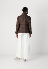 Veste matelassée marron avec col et manches longues, associée à un pantalon blanc évasé et des bottines beiges.