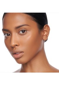 Nära bild av ett ansikte med medium hudton, slät textur, fylliga läppar och mörkt hår slickat bakåt, med naturlig make-up och klar hy.