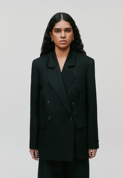 Schwarzes, doppelt knopfbares Blazer mit spitzem Revers, strukturierten Schultern und zwei vorderen Taschen. Weiche Textur und Knopfdetails sind vorhanden.