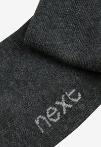 Dunkelgraue Socken mit einem strukturierten Strickmuster, das auf der einen Seite ein weißes "next"-Logo aufgestickt hat. Der Stoff wirkt weich und langlebig.
