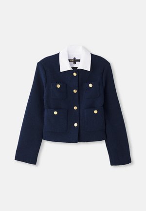 Giacca cropped blu navy in tessuto testurizzato con colletto bianco, dotata di chiusure a bottone dorato e quattro tasche frontali.