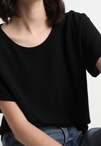 Zwarte top met korte mouwen en een ronde halslijn, met een gladde textuur en een relaxte pasvorm, gecombineerd met spijkerbroeken.