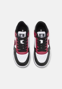 Sneakers med vit bas, svarta detaljer och vinröda överlägg. Har runda skosnören, perforeringar och en logotyp på tungan.