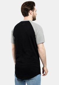 Juodas ir pilkas trumpo rankovės T-shirt su suapvalintu kraštu, turintis raglano dizainą ir tekstūruotą medžiagą ant pečių.