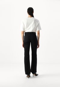 Camisa branca de manga curta e jeans pretos boca de sino. Os jeans têm bolsos traseiros e um cinto preto, com sapatos de salto agudo pretos.