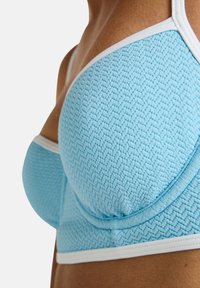 Light blue bra featuring a textured pattern, white trim, and a structured design with molded cups for support.