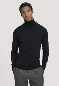 Schwarzer Rollkragenpullover in einem taillierten Design mit langen Ärmeln, aus glattem Strickstoff gefertigt, kombiniert mit hellgrauen Hosen.