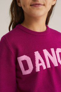 Fuksijas adīts džemperis ar apaļu apkakli, kurā priekšā lieli rozā burti veido vārdu "DANCE", gluda tekstūra un ribotas piedurknes.