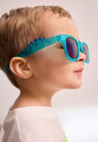 Blaue Sonnenbrille mit einzigartigem Dinosaurier-Design an den Seiten, ausgestattet mit dunklen Gläsern und einem durchsichtigen Gestell.