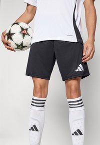 Crne sportske kratke hlače s bijelim Adidas logotipom, uparene s bijelim čarapama do koljena koje imaju crne pruge, te crno-bijela nogometna lopta.