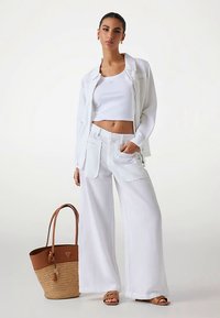 Ensemble en lin blanc comprenant un top court et un pantalon large, assorti à un sac fourre-tout marron tressé et des sandales camel.