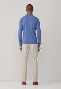 Svetlomodré tričko s dlhým rukávom a golierom, doplnené o svetlo béžové nohavice a hnedú obuv. Hladká textúra a priliehavý strih.