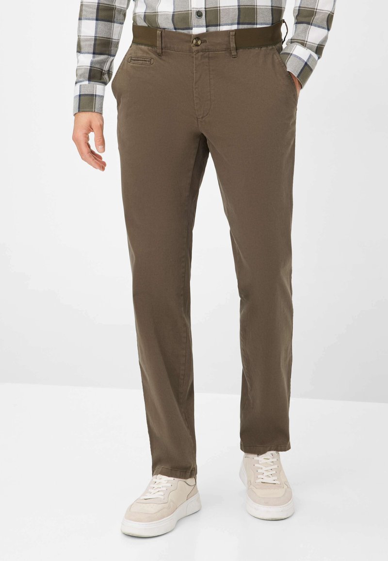 Pantaloni in cotone marrone con vestibilità slim, dotati di tasche laterali, chiusura con bottone e una superficie liscia, abbinati a sneaker chiare.