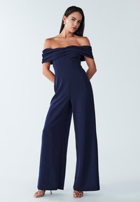 Marineblauwe off-shoulder jumpsuit met geplooide lijfje, wijde benen en een aansluitende taille. Gemaakt van gladde stof met een subtiele glans.