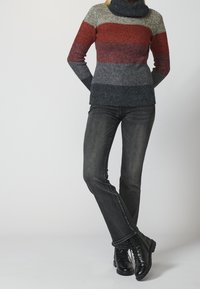 Pull en tricot avec un col montant ; présente des rayures horizontales rouges, grises et noires. Associé à un jean en denim noir et des bottes noirs à lacets.