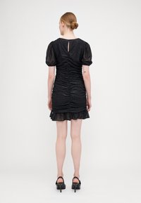 Robe mini noire avec un design texturé et froncé, manches ballons, dos en forme de clé et ourlet volanté. Fabriquée dans un tissu scintillant. Chaussures à talons.