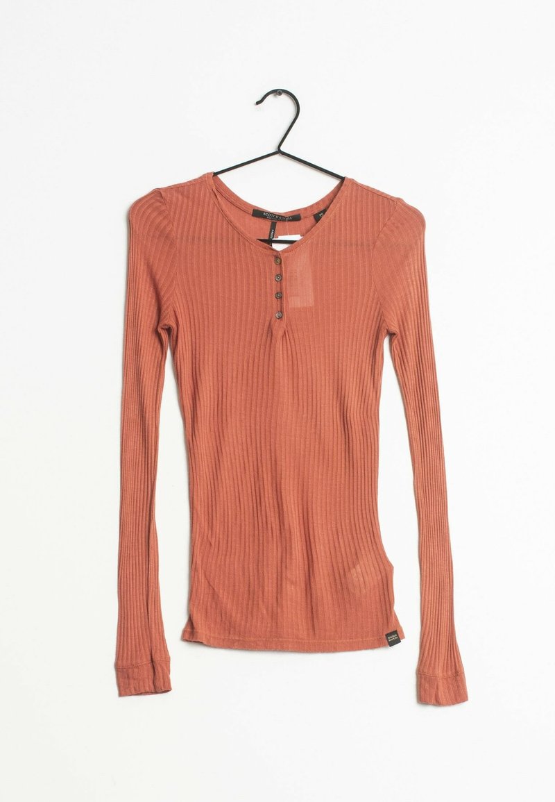 Långärmad ribbad topp i terrakotta med rund halsringning, fyra knappar och en liten etikett nära nederkanten.