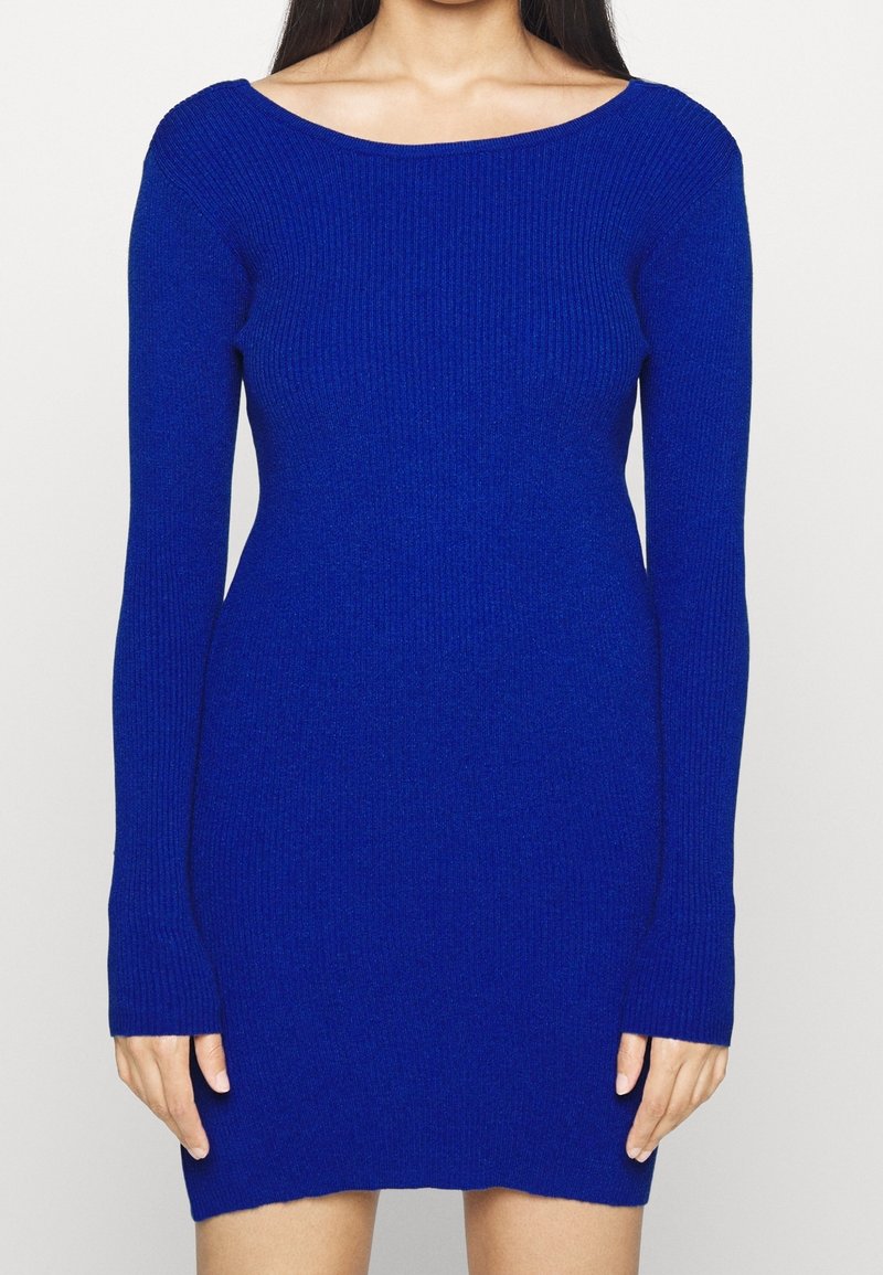 Pletené šaty v živé modré barvě, s širokým výstřihem, dlouhými rukávy, přiléhavým střihem a žebrovanou texturou. Spodní lem končí těsně nad středem stehna.