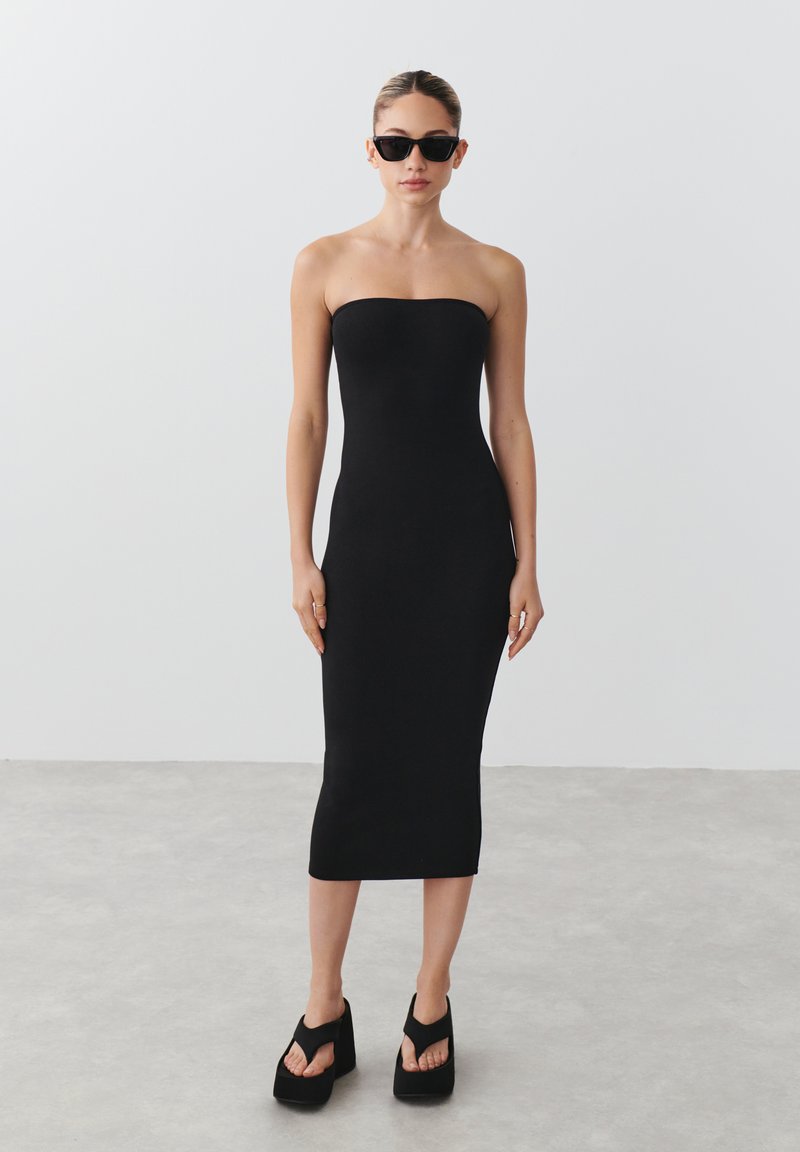 Juoda be petnešų midi suknelė, pagaminta iš tamprios medžiagos, prigludusi siluetas, lygi tekstūra. Sujungta su masyviais platforminiais sandalais.