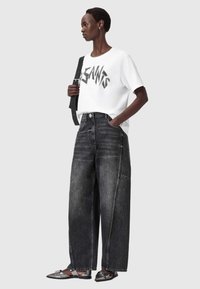 T-shirt bianca con testo grafico nero, abbinata a jeans in denim nero a gamba larga con tasca frontale e cucitura a contrasto.