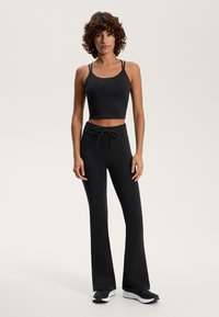 Čierny krátky top s tenkými ramienkami v kombinácii s čiernymi rozšírenými nohavicami so sťahovacím pásom a jemnými kovovými detailmi.