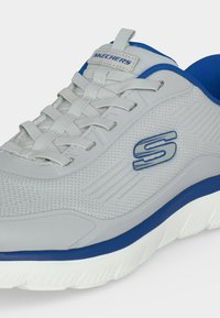 Ανοιχτογρι sneaker Skechers με μπλε λεπτομέρειες, επάνω μέρος από ύφασμα με δίχτυ, λευκά κορδόνια και παχιά λευκή σόλα με μπλε περίγραμμα.