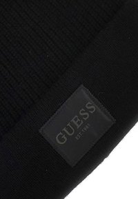 Beanie nera in maglia con un motivo strutturato e un'etichetta rettangolare nera cucita su cui è impresso in grigio "GUESS" e "EST.1981".