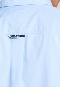 Himmelblaue Hemd mit einem Detail am Kragen auf der Rückseite. "HILFIGER"-Logo in schwarzer Stickerei auf einem Tab in der Mitte. Der Stoff wirkt glatt und frisch.