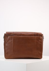 Sac messenger en cuir brun au design épuré, avec un rabat supérieur, une texture lisse et des poches zippées sur les côtés pour une fonctionnalité accrue.