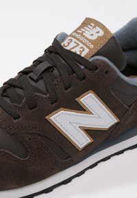 Baskets de sport marron en matériaux suédé et cuir. Présentent un logo blanc, des accents beiges sur la languette et une semelle noire texturée.