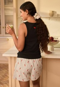 Black tank top with a red chili logo, paired with white striped shorts featuring red chili pepper patterns. Holding a green drink.