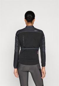 Čierna cyklistická bunda s úzkym strihom, elastickým pásom, textúrovanými rukávmi a zipsovým vreckom na zadnej strane. Hladká textura látky.