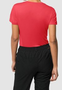 Person standing facing away wearing a fitted short-sleeve red shirt and black elastic-waist pants against a plain background.