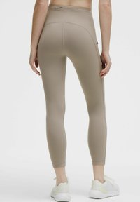 Beiga träningsleggings tillverkade av ett stretchigt material, med hög midja, sidofickor och en mjuk yta. Utsmyckade med reflekterande detaljer.