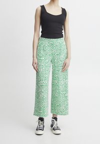 Svart ärmlös topp i kombination med vida byxor med ett grönt och vitt geometriskt mönster. Svarta högsnörda sneakers fulländar outfiten.