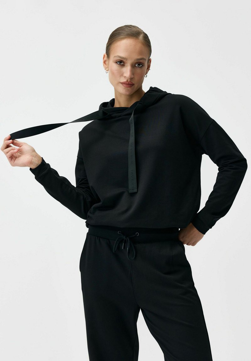Czarna krótka bluza z kapturem ze sznurkiem, o miękkiej teksturze i dopasowanych ściągaczach, w zestawie z czarnymi spodniami na miarę.