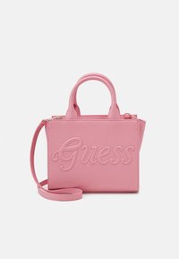 Sac à main en simili cuir rose avec logo "Guess" embossé, double anses supérieures et une bandoulière détachable. Forme rectangulaire et texture lisse.