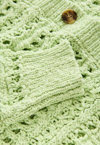 Cardigan en coton vert clair, avec un motif ouvert texturé et des poignets côtelés solides, orné d'un bouton rond marron.