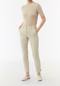 Beige åtsittande topp med korta ärmar, i kombination med ljusbeige skräddarsydda byxor som har fickor och en subtil slits vid fållen.