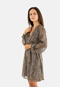 Robe mini à motifs marron et noir avec un décolleté en V profond, des manches longues, une taille élastique et une texture de tissu fluide et léger.