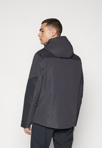 Casaco impermeável preto com capuz ajustado, apresenta uma textura suave, design de painéis contrastantes e punhos ajustáveis.