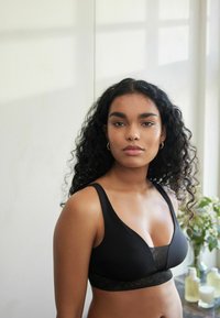 Reggiseno nero in tessuto morbido, con un particolare in pizzo nella parte inferiore. Coppe morbide con spalline larghe, progettato per comfort e supporto.