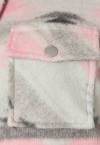 Tissu en polaire aux nuances de gris, rose et blanc, avec une poche plaquée ornée d'un bouton-pression argenté. Surface texturée et douce.