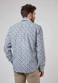 Chemise à manches longues avec un motif floral bleu sur fond blanc. Col boutonné, ourlet courbé et coupe ajustée.